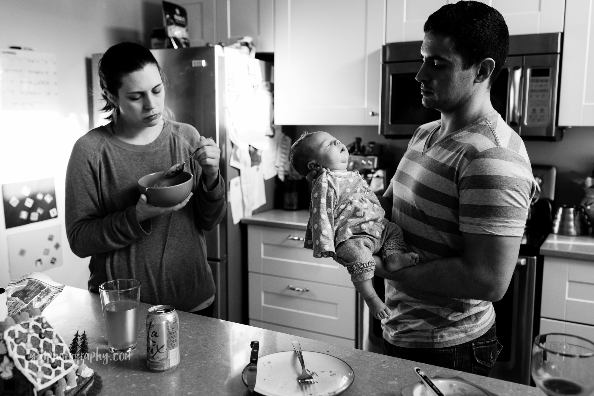seattle mom eating quick lunch while husband holds newborn baby