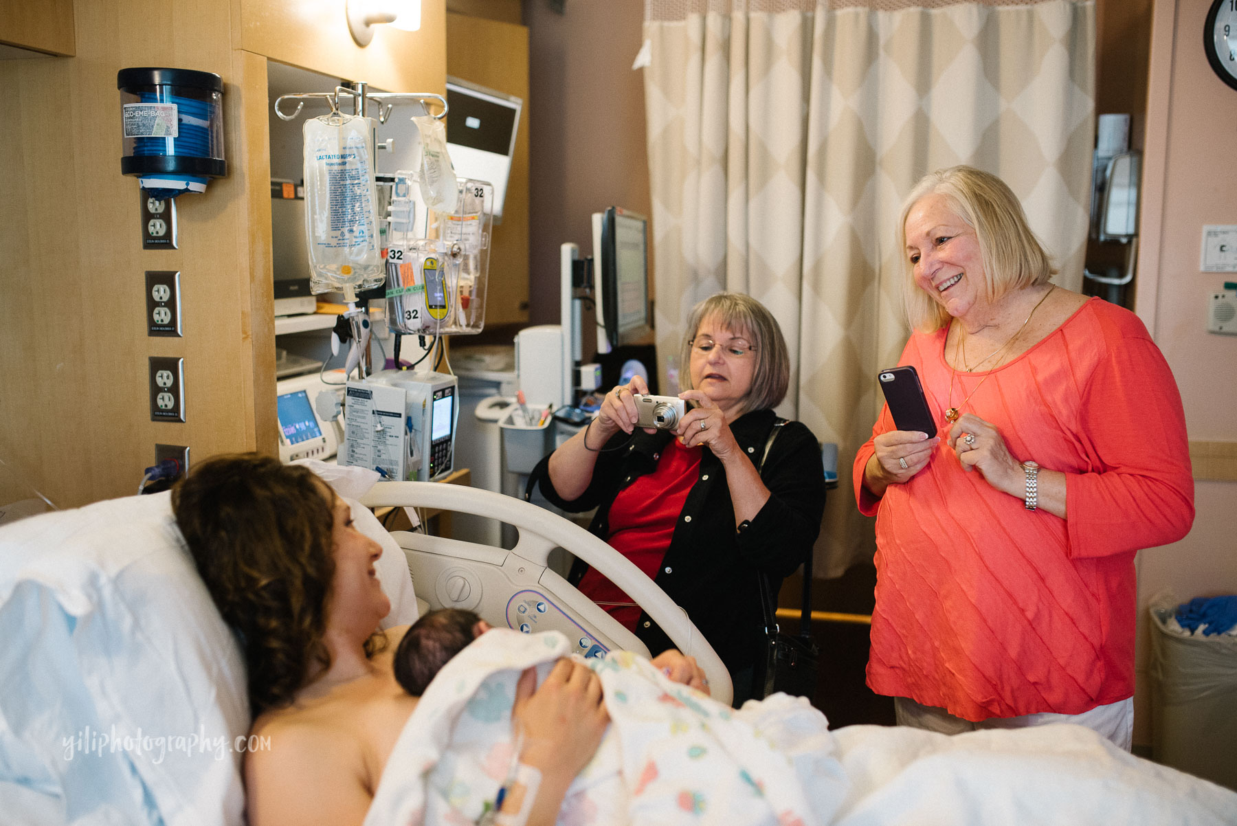 two grandmothers taking photos of their granddaughter after birth in hospital room