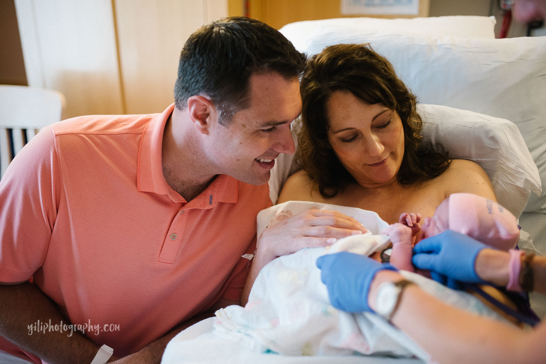 mom and dad in hospital room with newborn baby girl admiring her