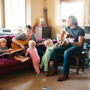 Mom and dad playing guitars and singing with twins and older son in living room