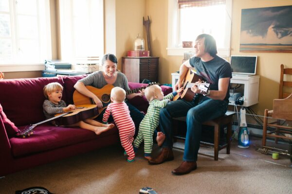 Mom and dad playing guitars and singing with twins and older son in living room