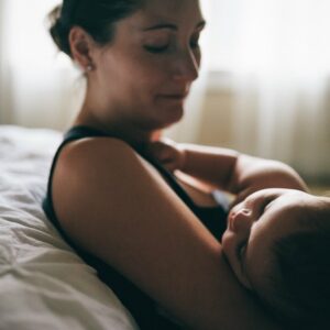 Mom holding sleeping baby against bed