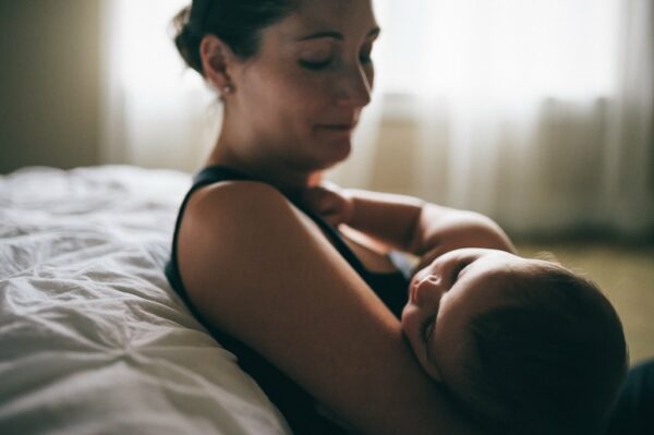 Mom holding sleeping baby against bed