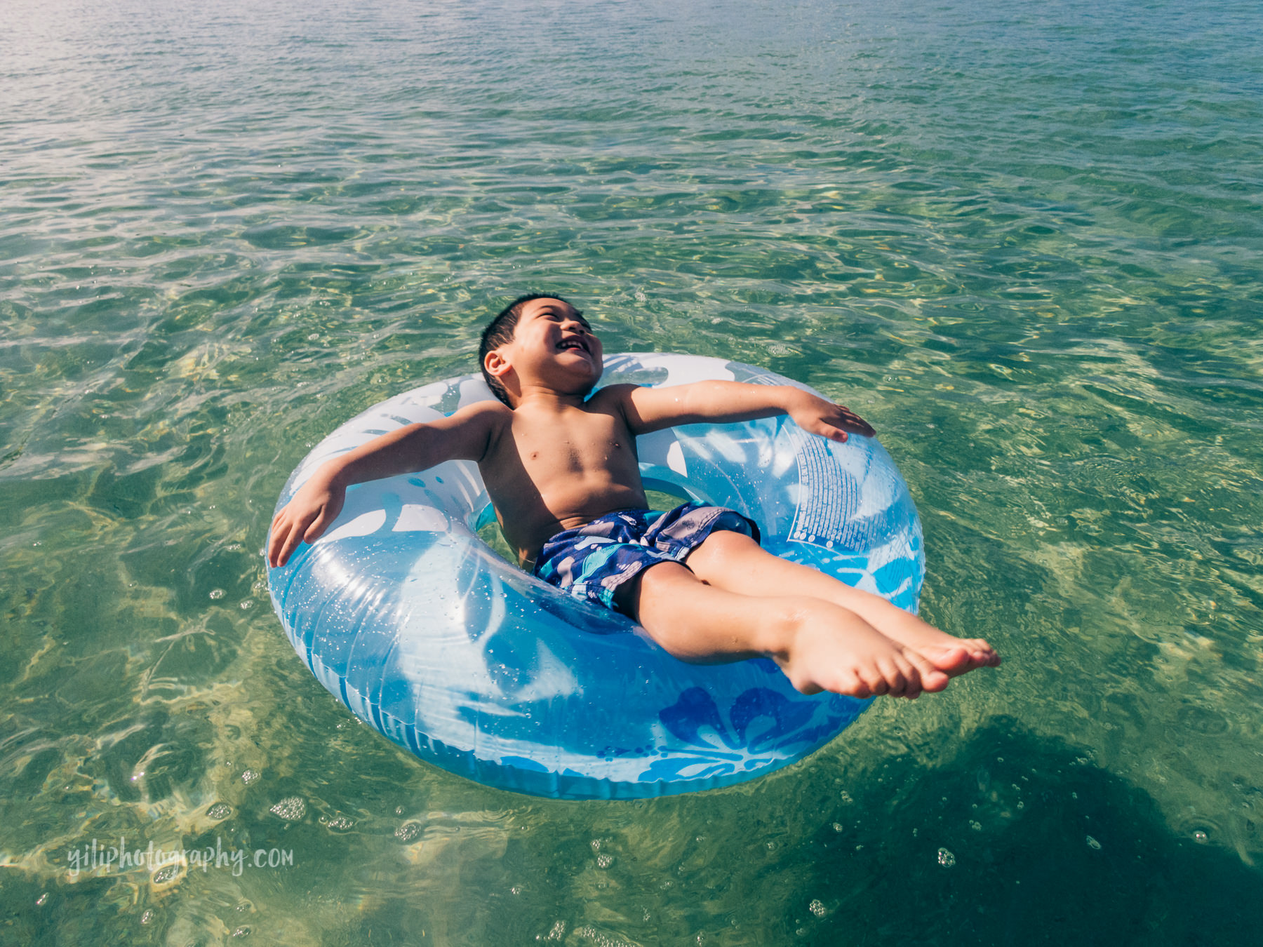 toddler boy laughing in floatie in ocean