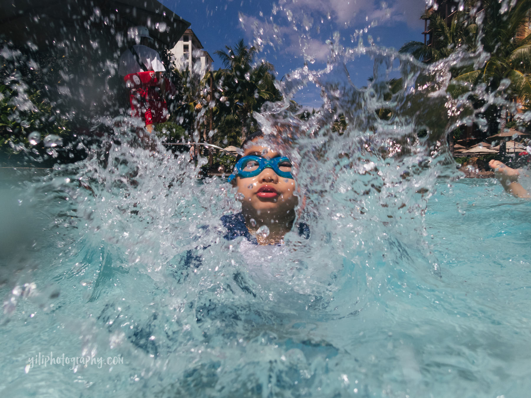 boy splashing water at camera in pool 