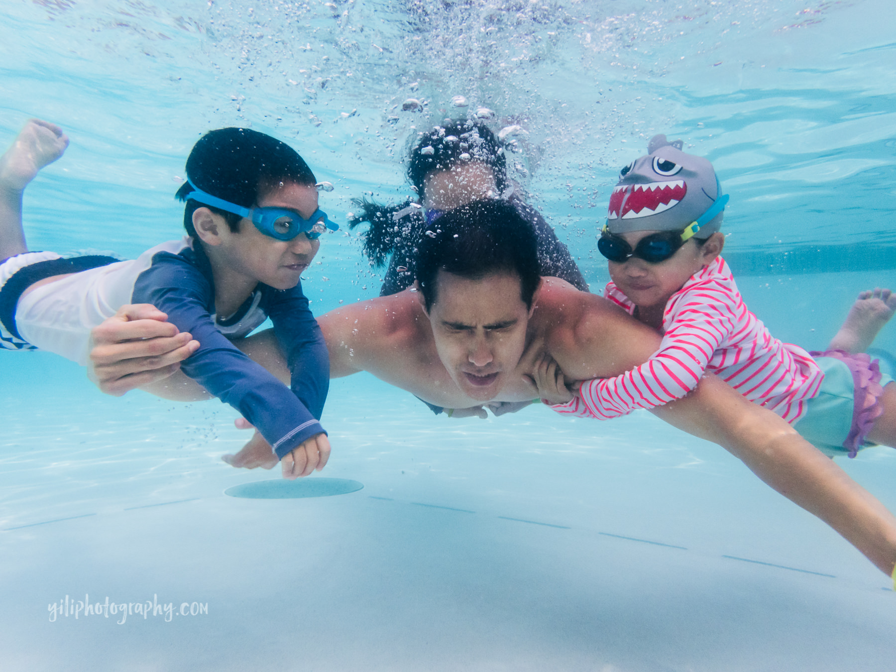 father swimming underwater with three kids holding him