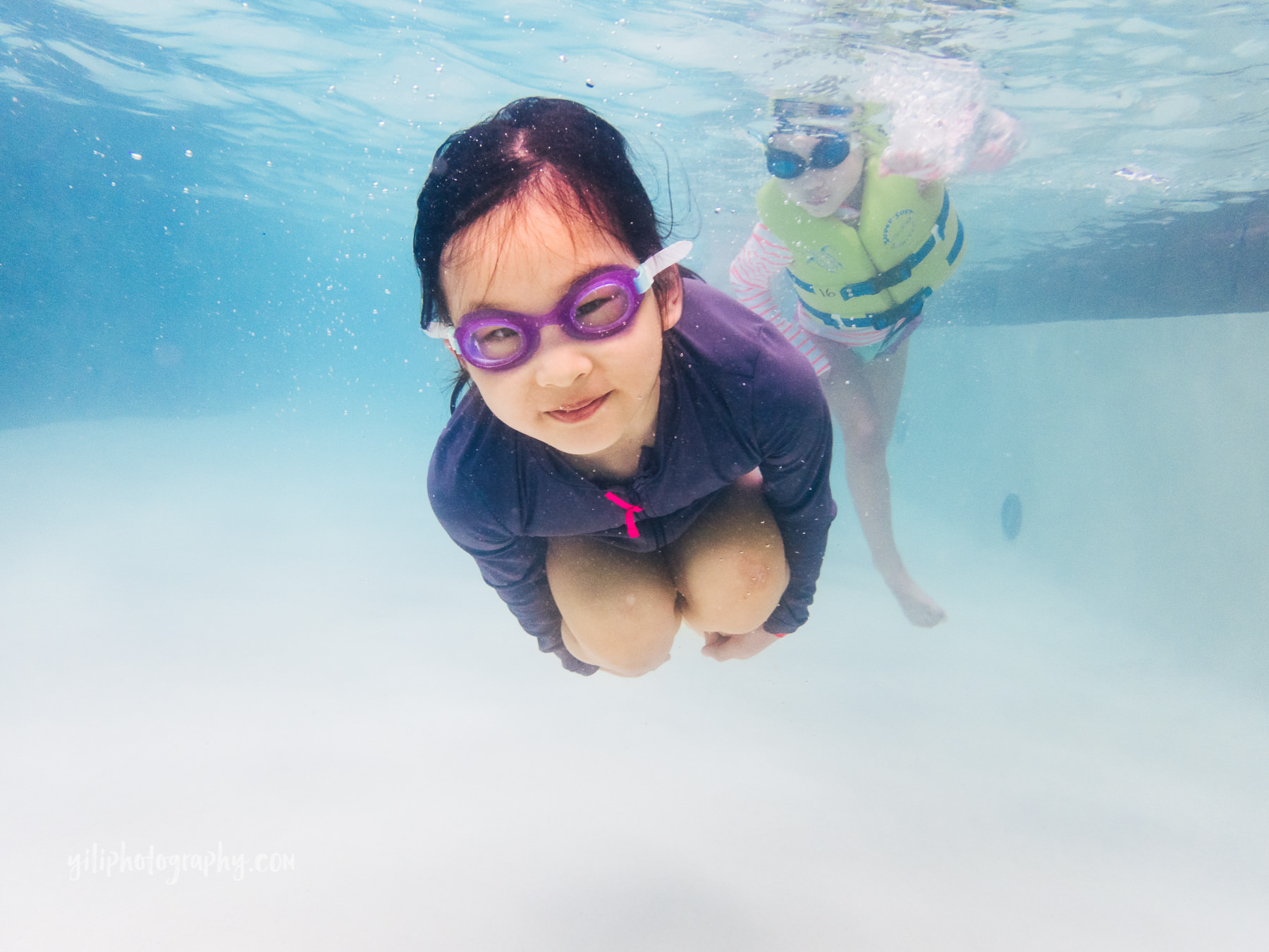 underwater photo of girl in goggles tucked in ball