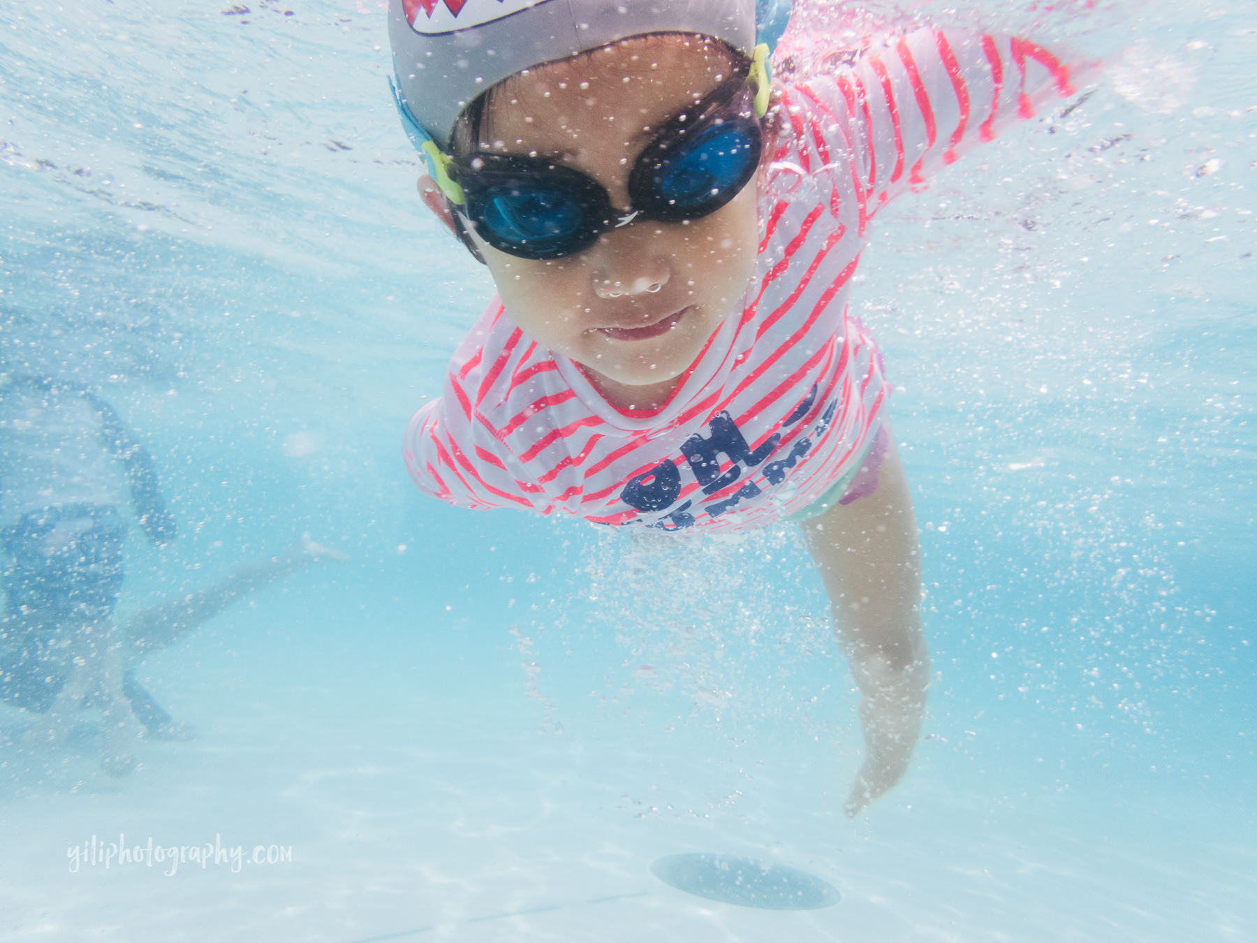 little girl in swim cap and goggles swimming underwater