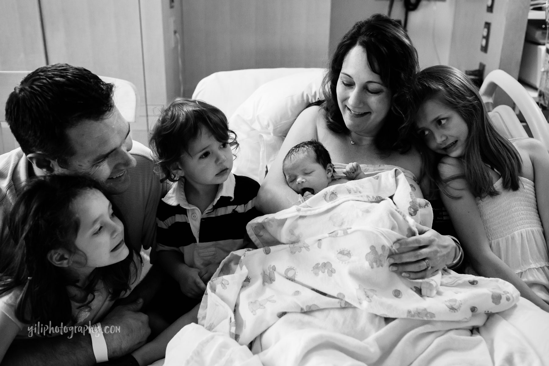 family with three siblings meeting newborn baby sister in hospital