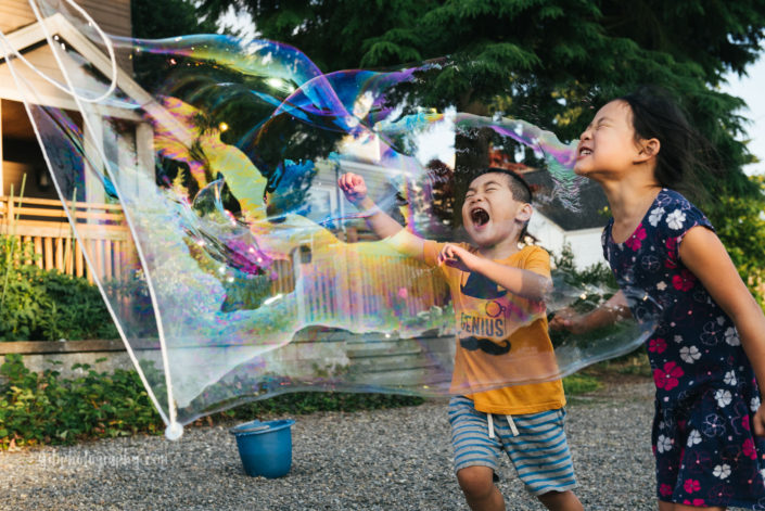 boy with big grin popping giant bubble with sister
