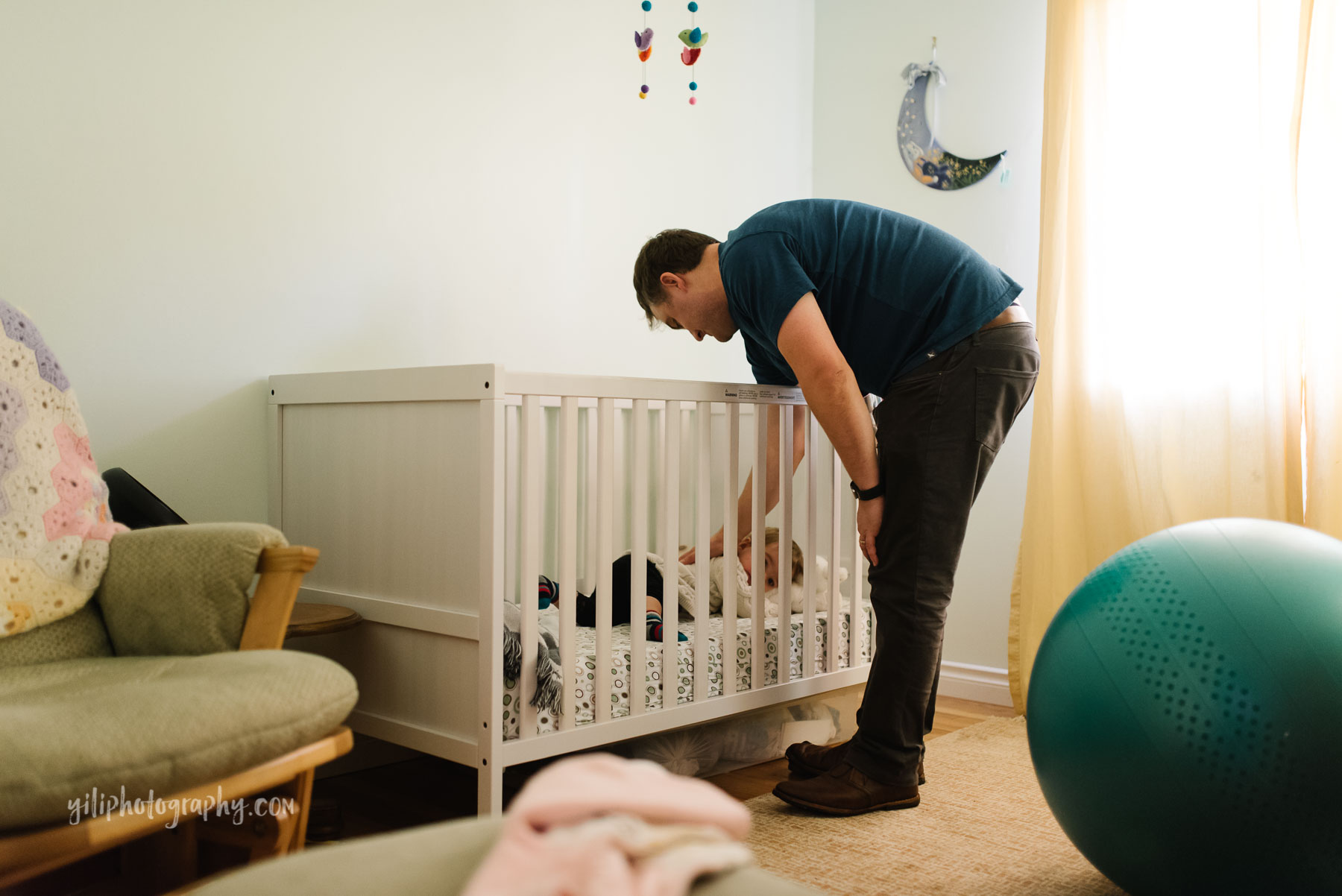 Father patting toddler girl's back in crib in nursery