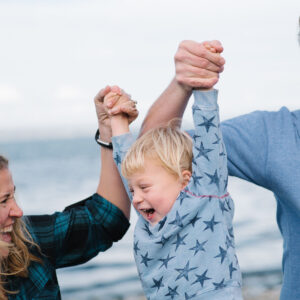 Caucasian parents swinging toddler boy at beach