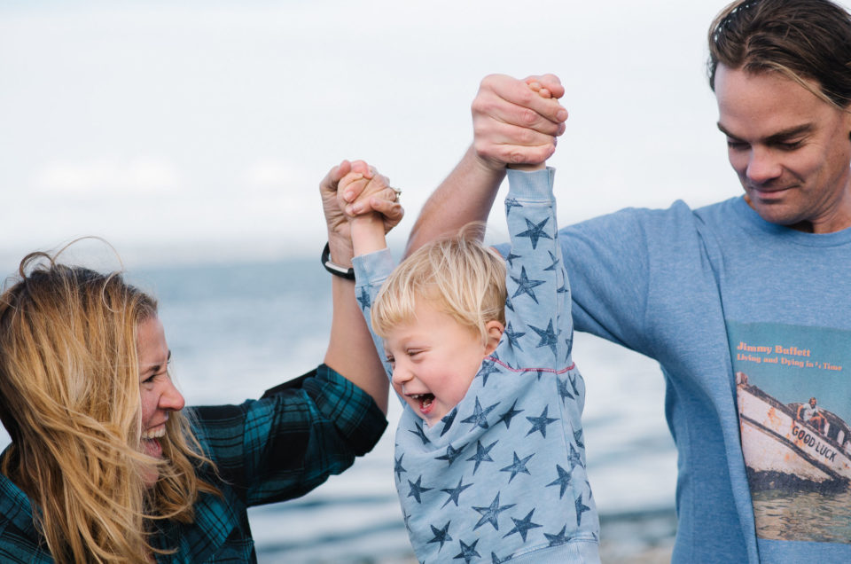 Caucasian parents swinging toddler boy at beach