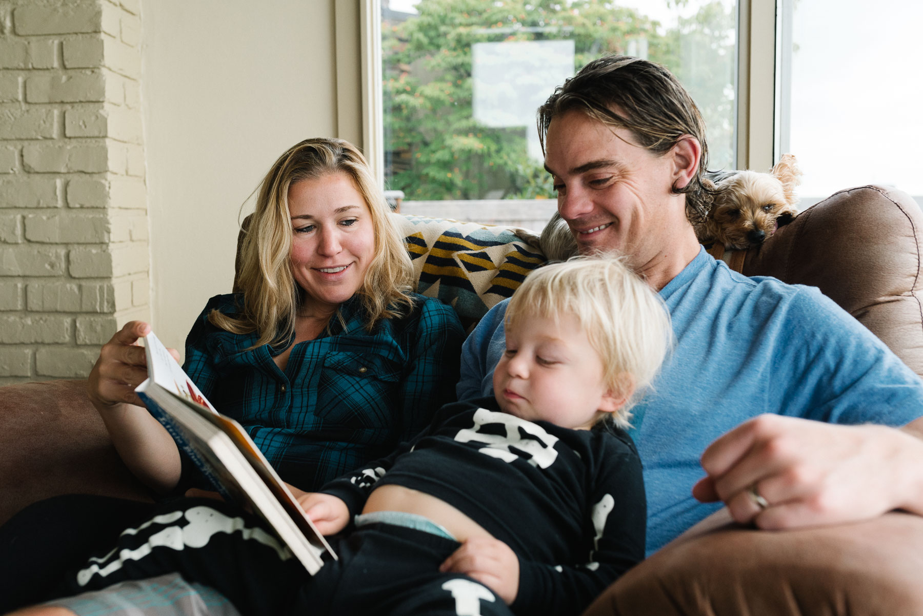 Mom and dad sitting on couch reading to toddler son