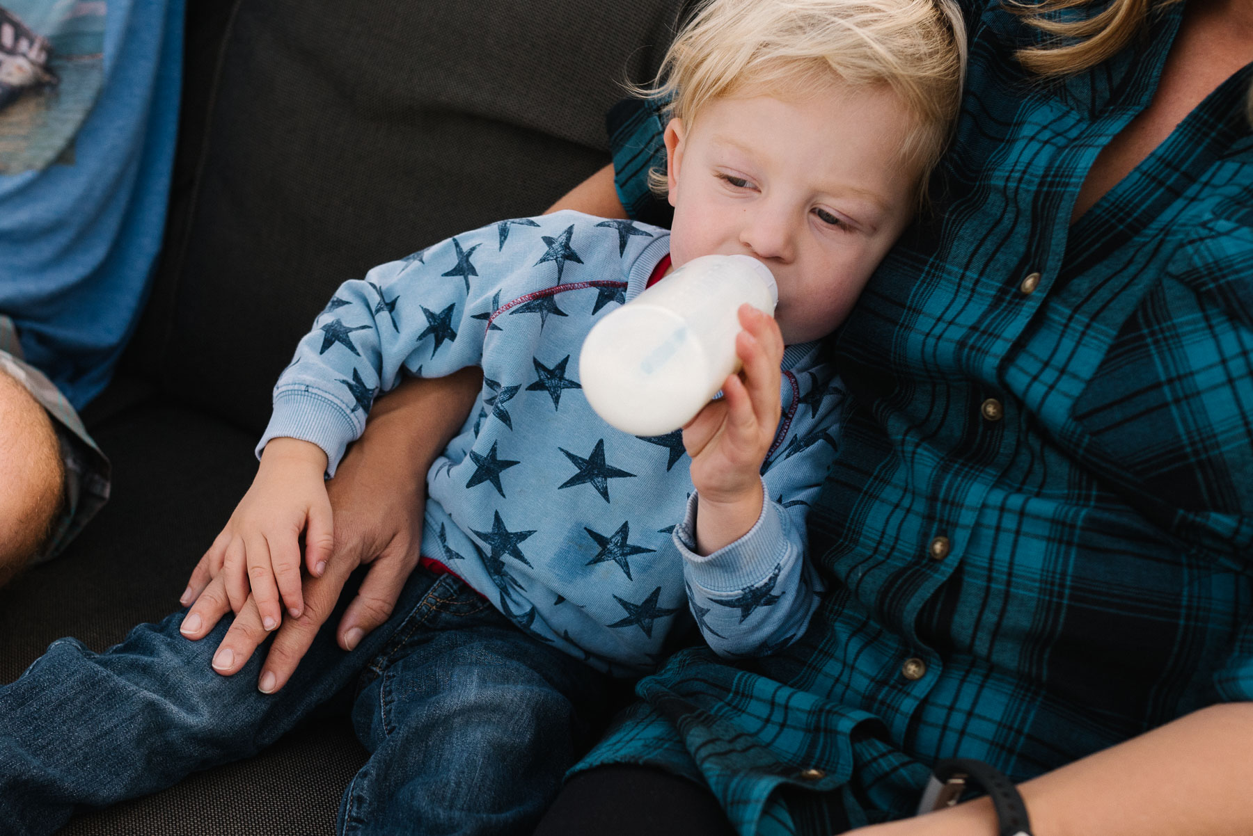 Toddler boy drinking milk from bottle cuddling with mom