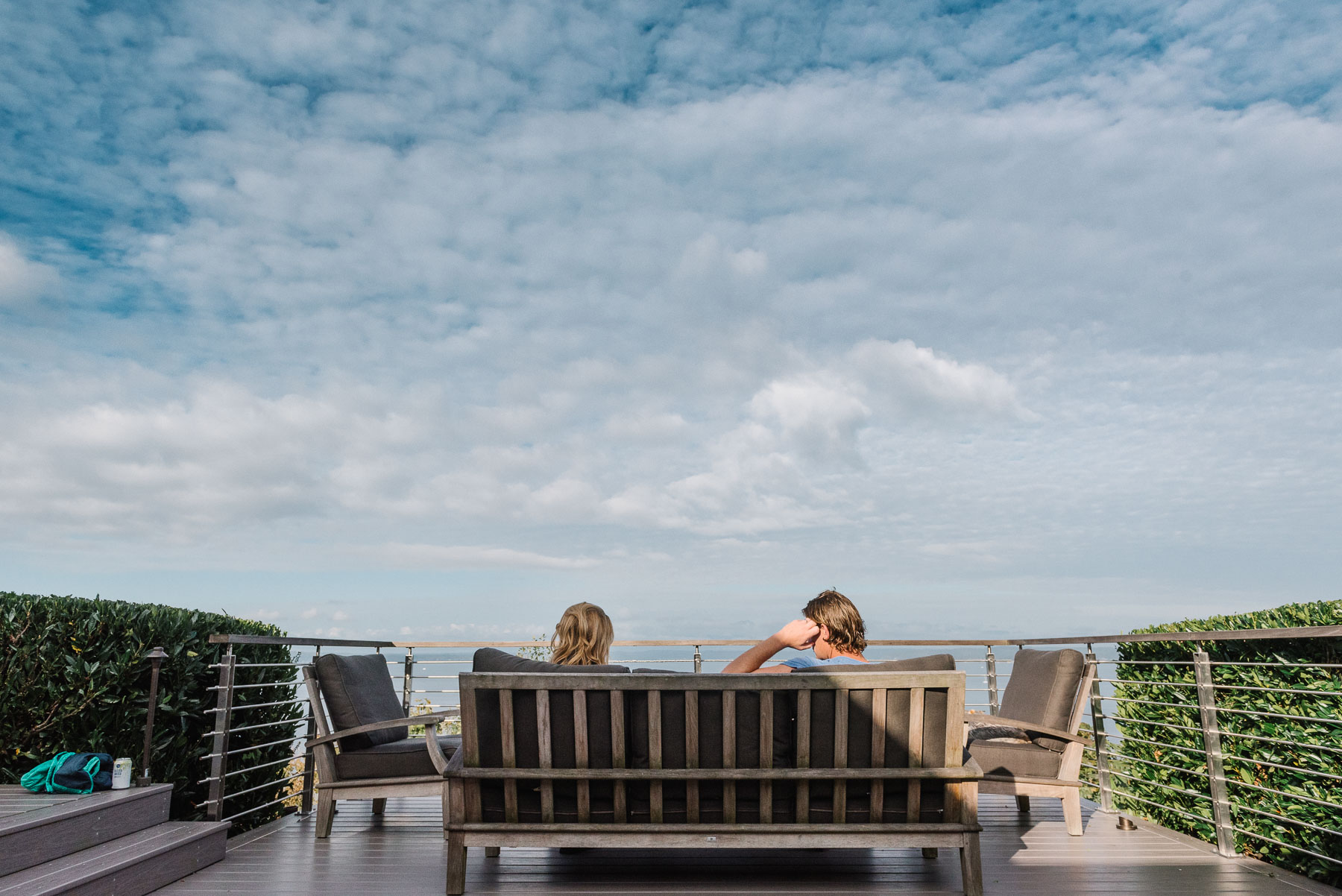Wide angle view of family sitting on patio furniture outside on sunny day overlooking ocean