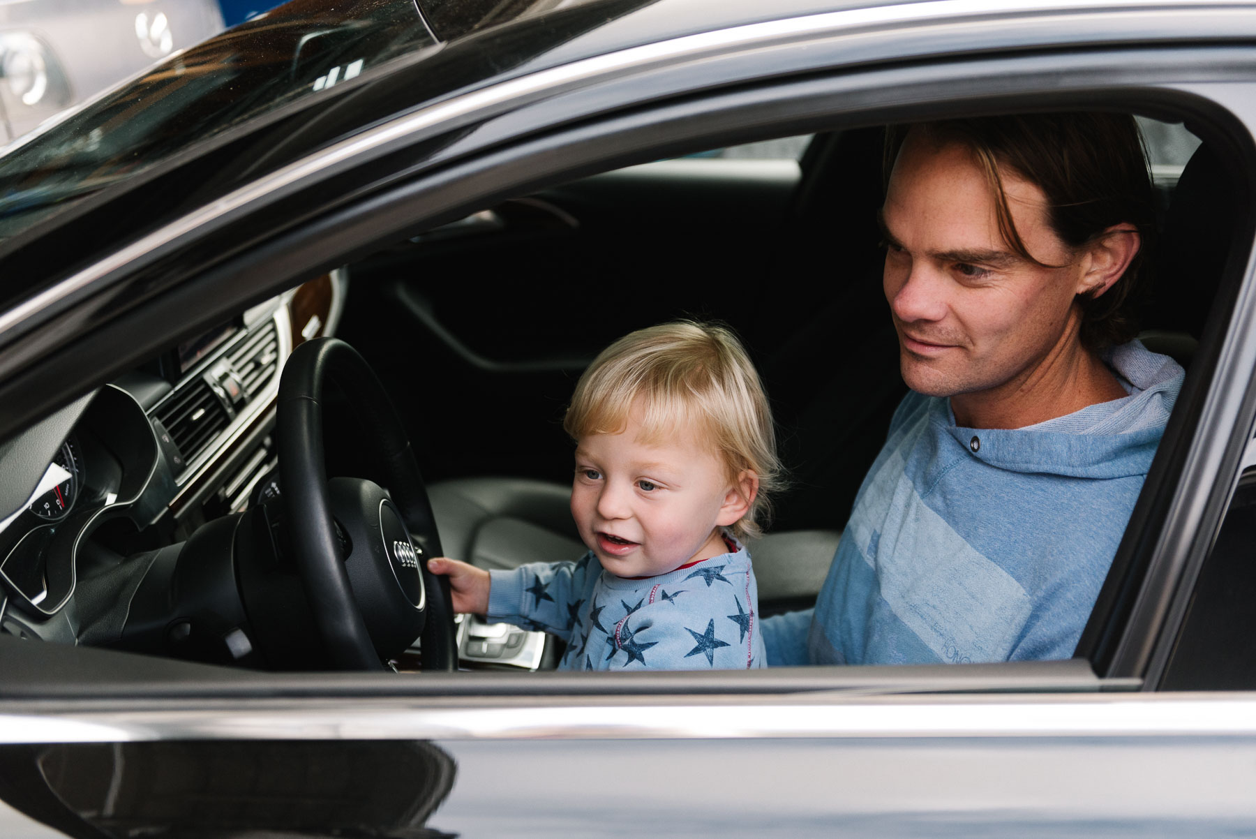 Toddler boy sitting on dad's lap in drivers seat of car