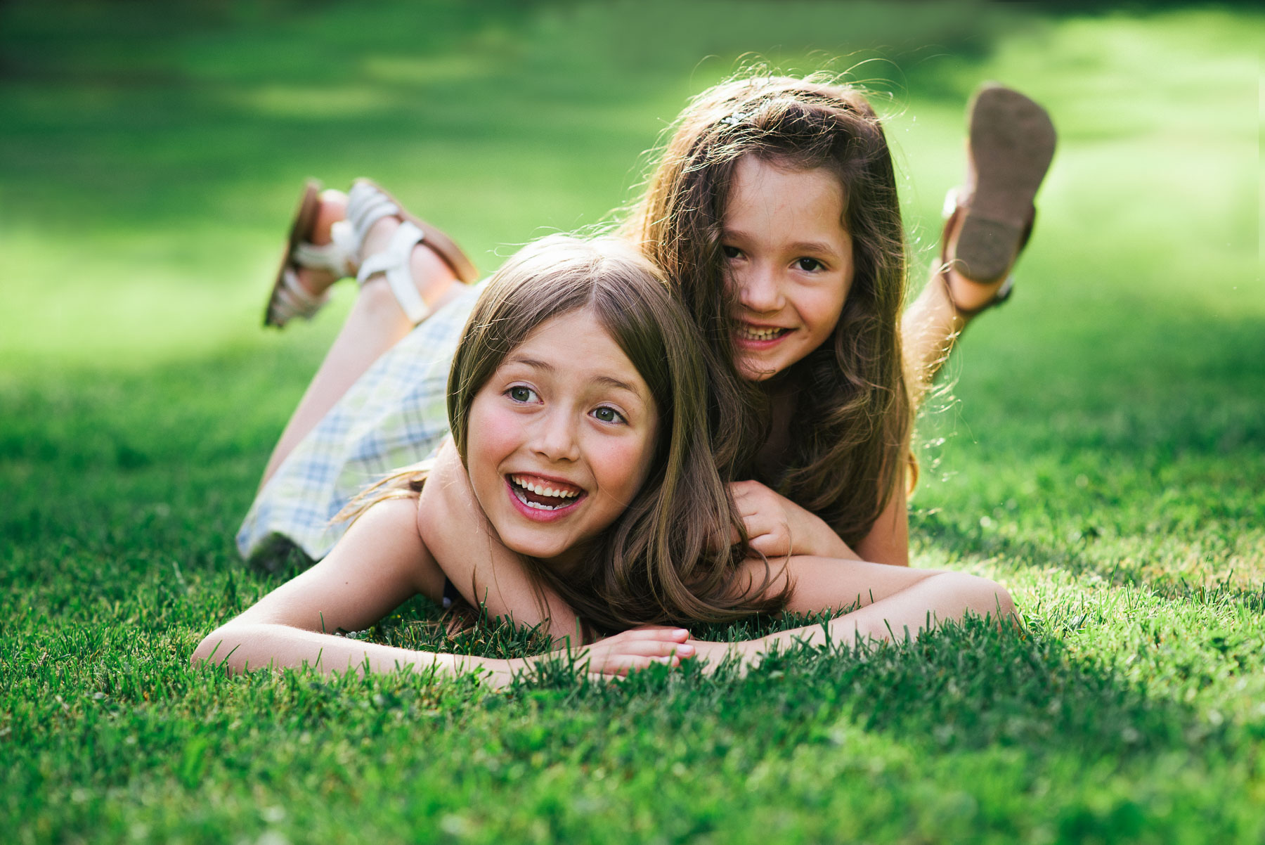 Two sisters laying on stomachs in grass acting silly