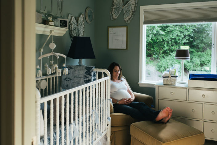 Serene expecting mother sitting in armchair in nursery holding belly