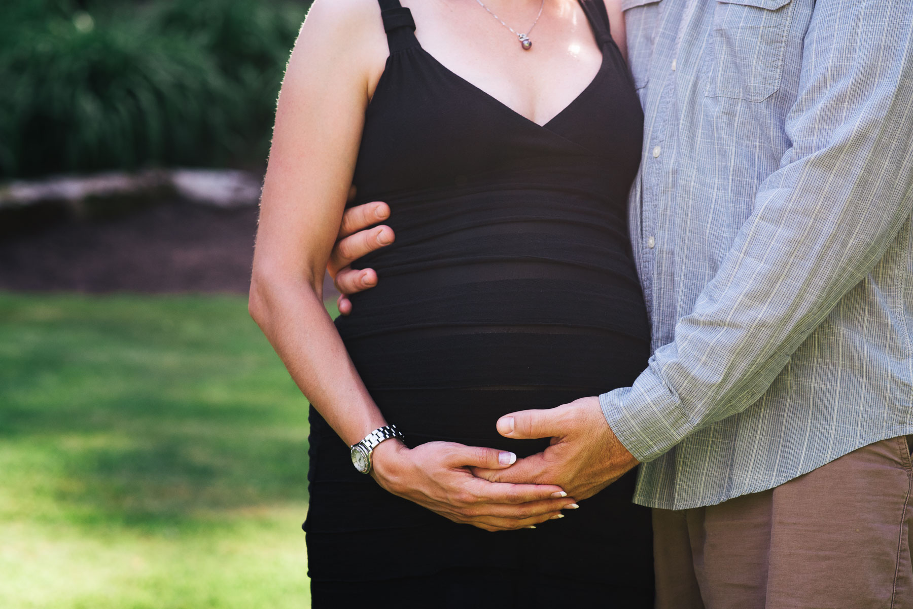 close up headless photo of expectant mom holding her belly while husband has arms wrapped around her