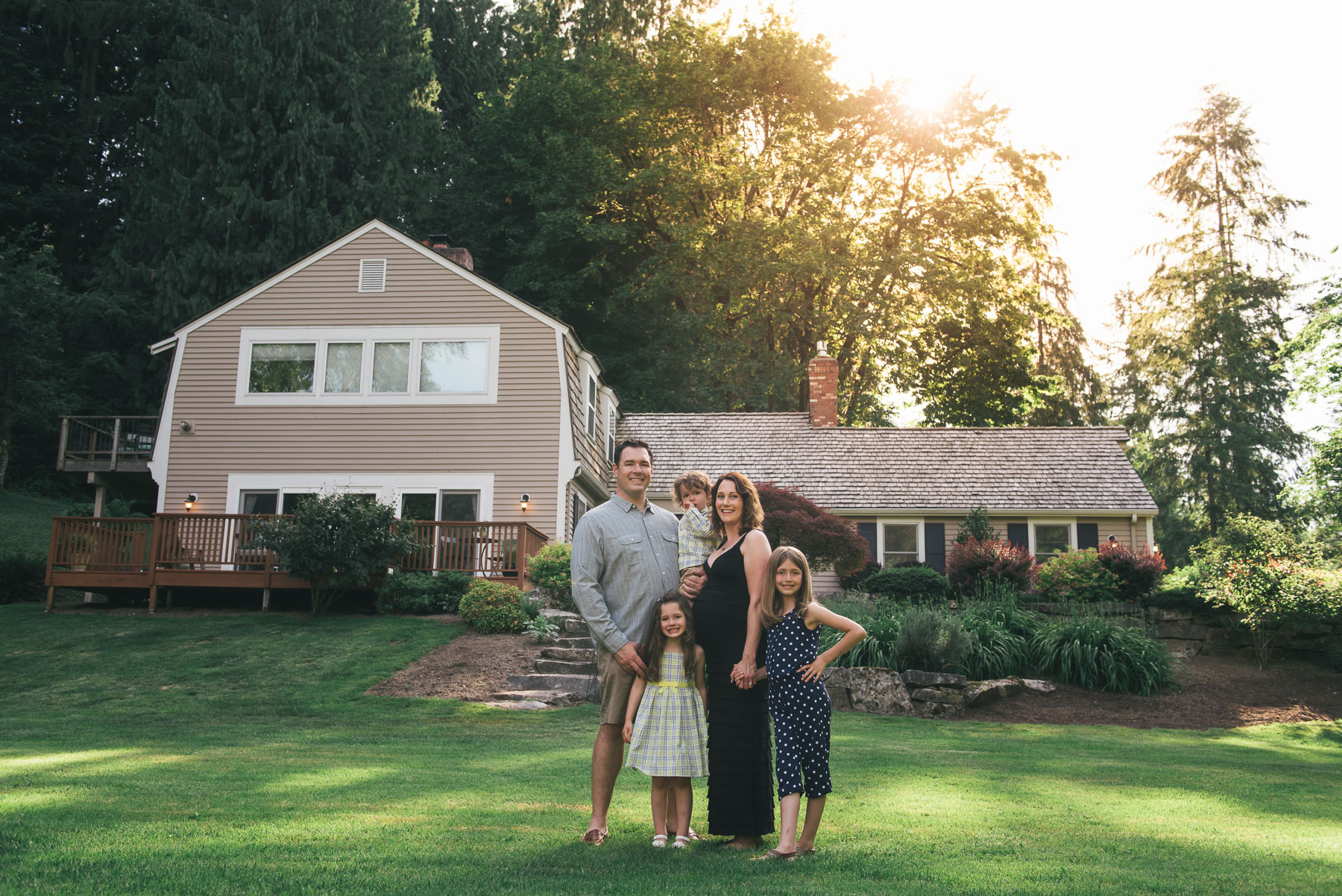 family of 5 posing in their front yard in front of house in late afternoon sunlight