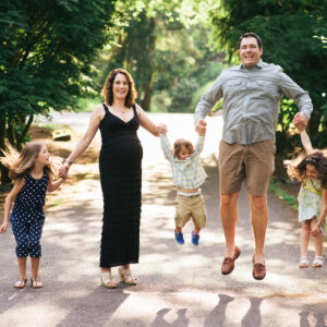 Family of 5 in their yard holding hands jumping