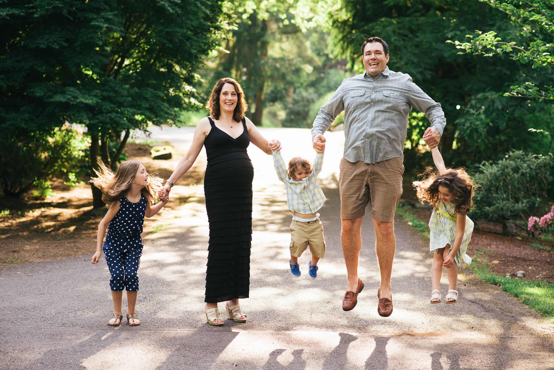 Family of 5 in their yard holding hands jumping