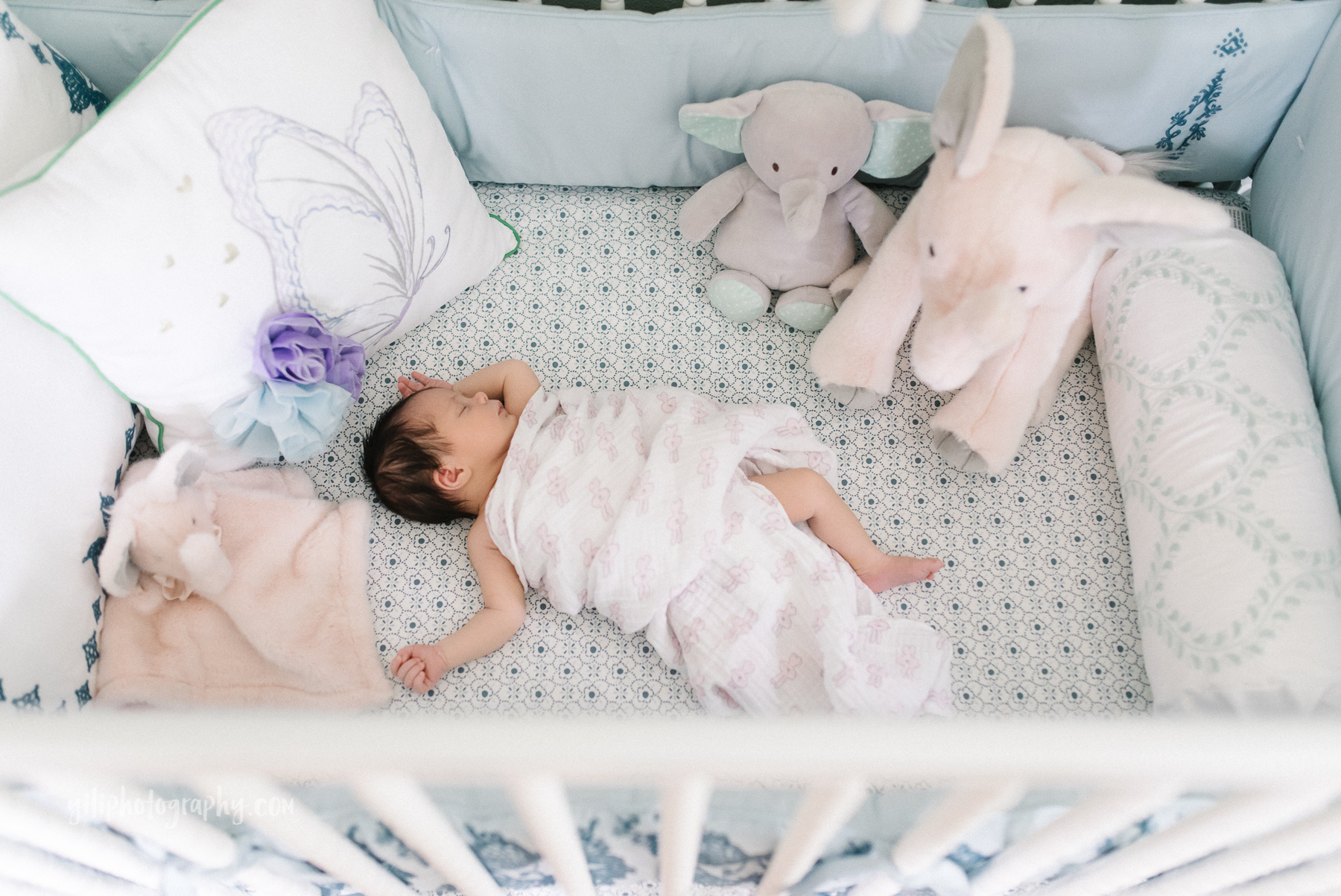 brunette newborn sleeping in crib wrapped in swaddle