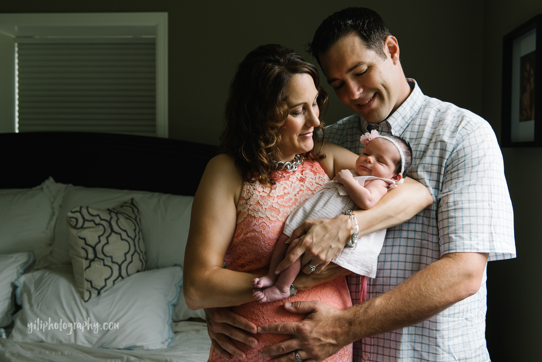 husband and wife smiling while holding newborn baby girl in their bedroom