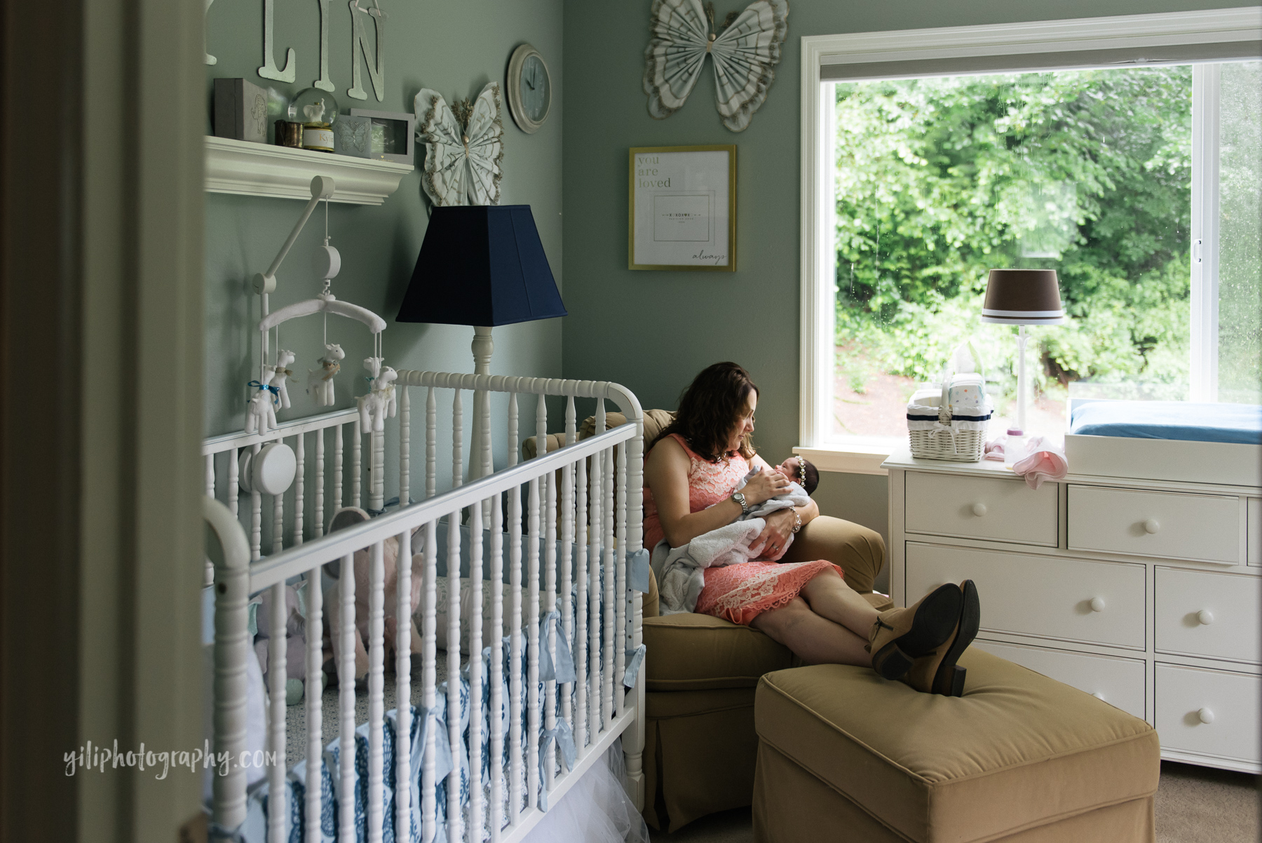 wide angle photo of mom sitting in rocker in nursery holding newborn