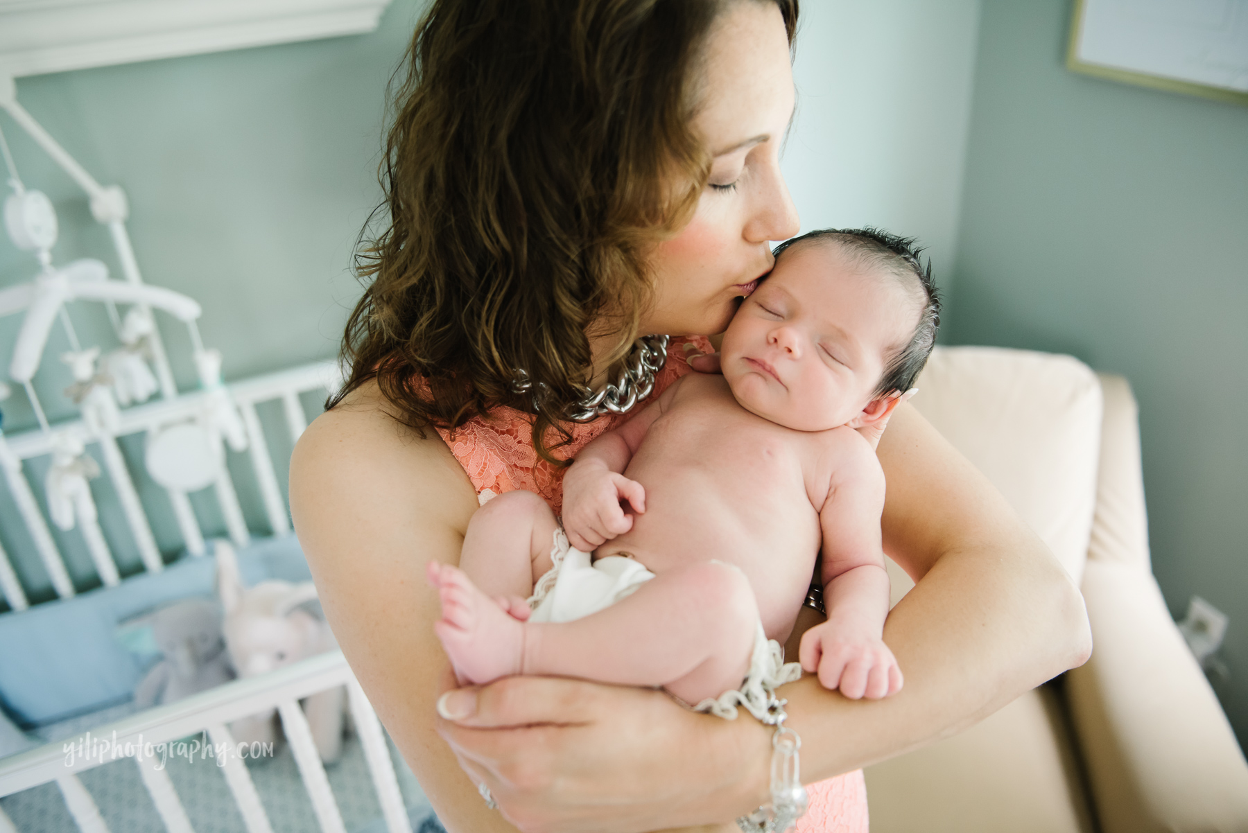 close up of mother giving newborn baby girl a kiss on her forehead in nursery