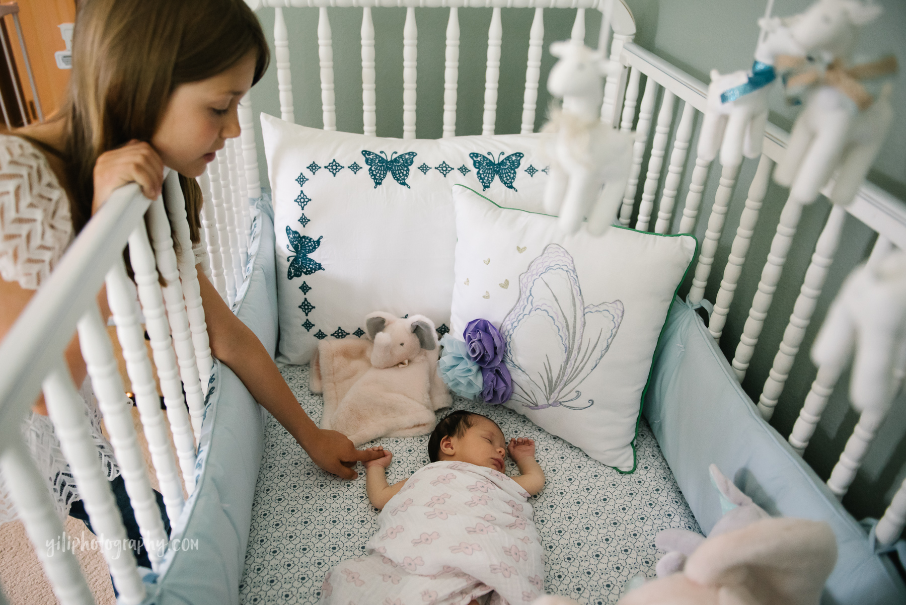 big sister touching hand of newborn baby girl while she sleeps in crib