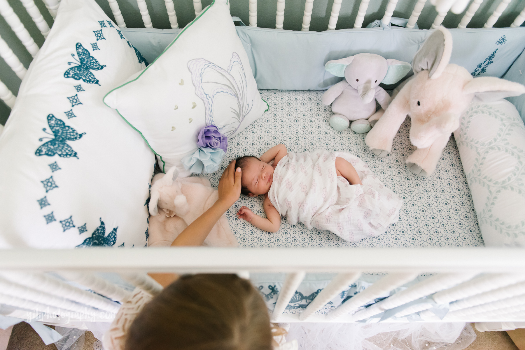 top down photo of big sister patting newborn girl's head in crib