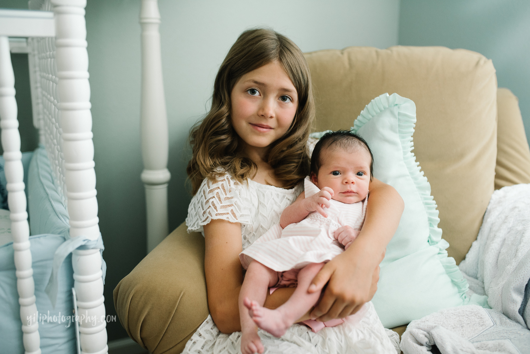 elementary school girl holding newborn baby sister in armchair