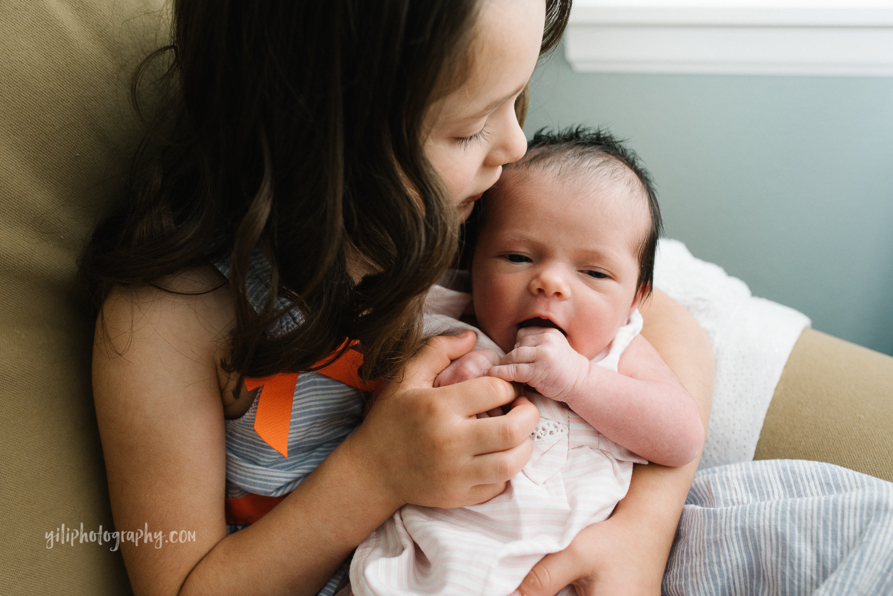 older sister giving newborn baby sister a kiss on forehead