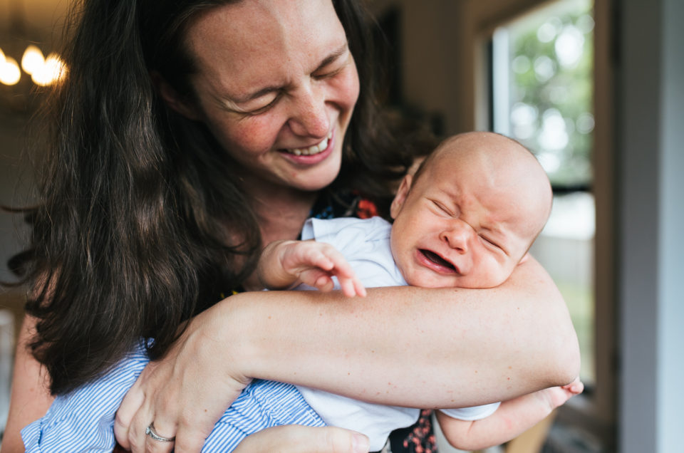 mom laughing while holding newborn son crying