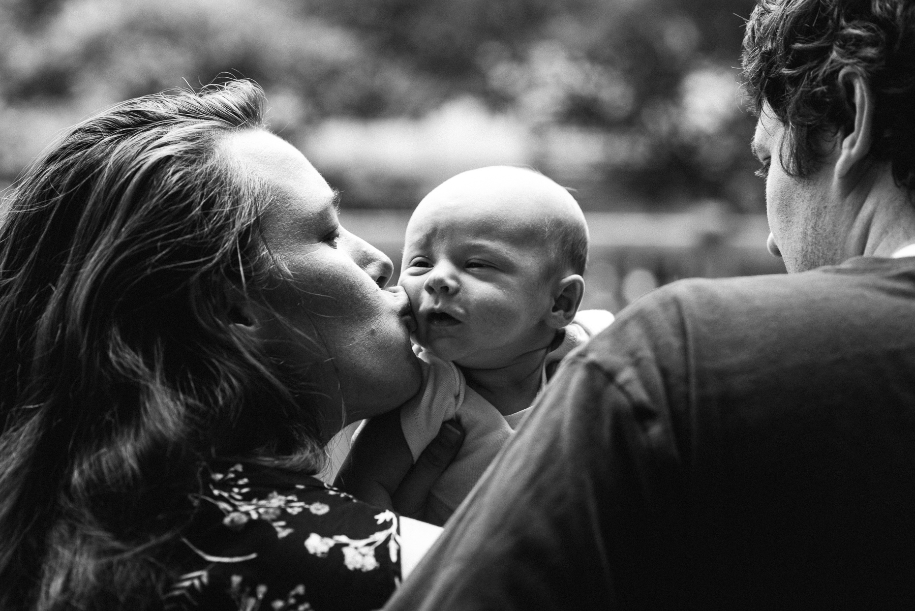 black and white photo of mom kissing newborn baby over dad's shoulder