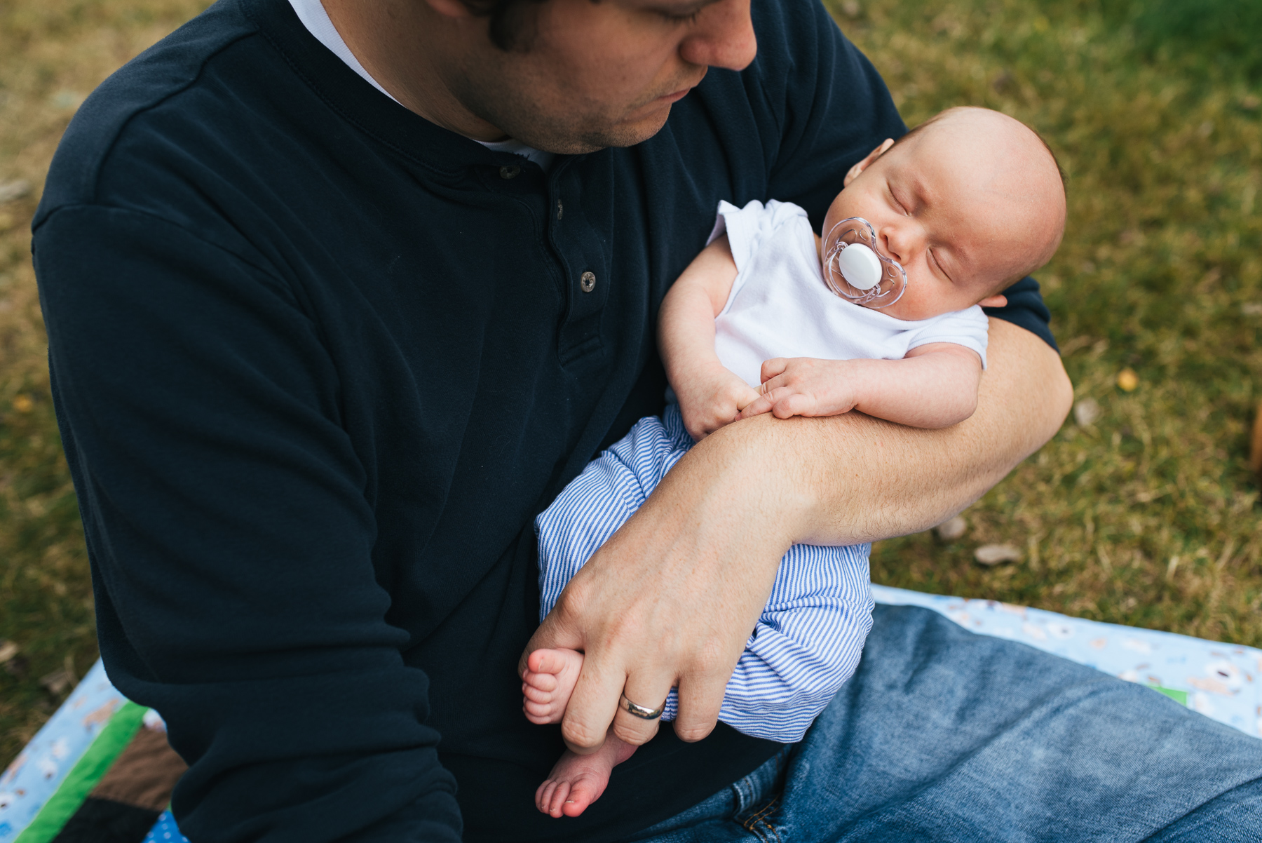 new father holding his sleeping newborn son with pacifier in yard