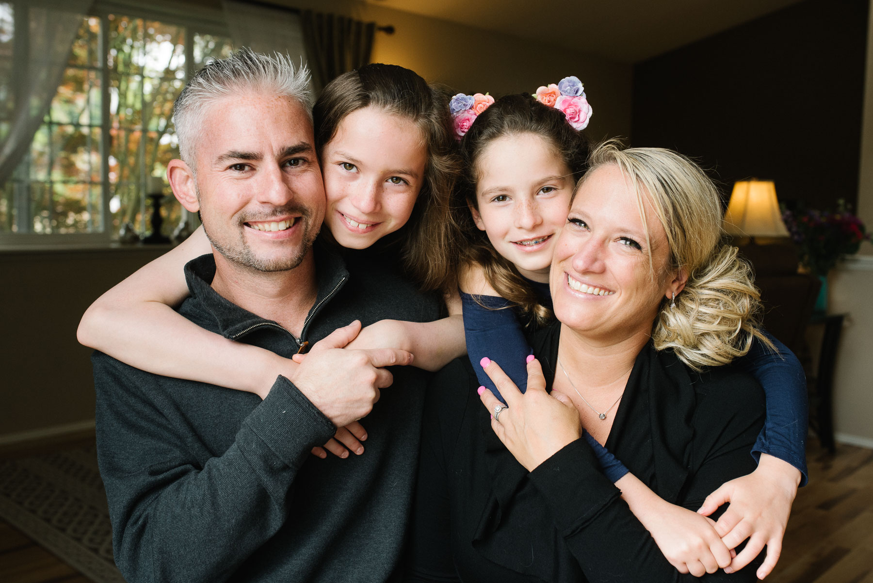 mother and father and two daughters with arms around shoulders in home