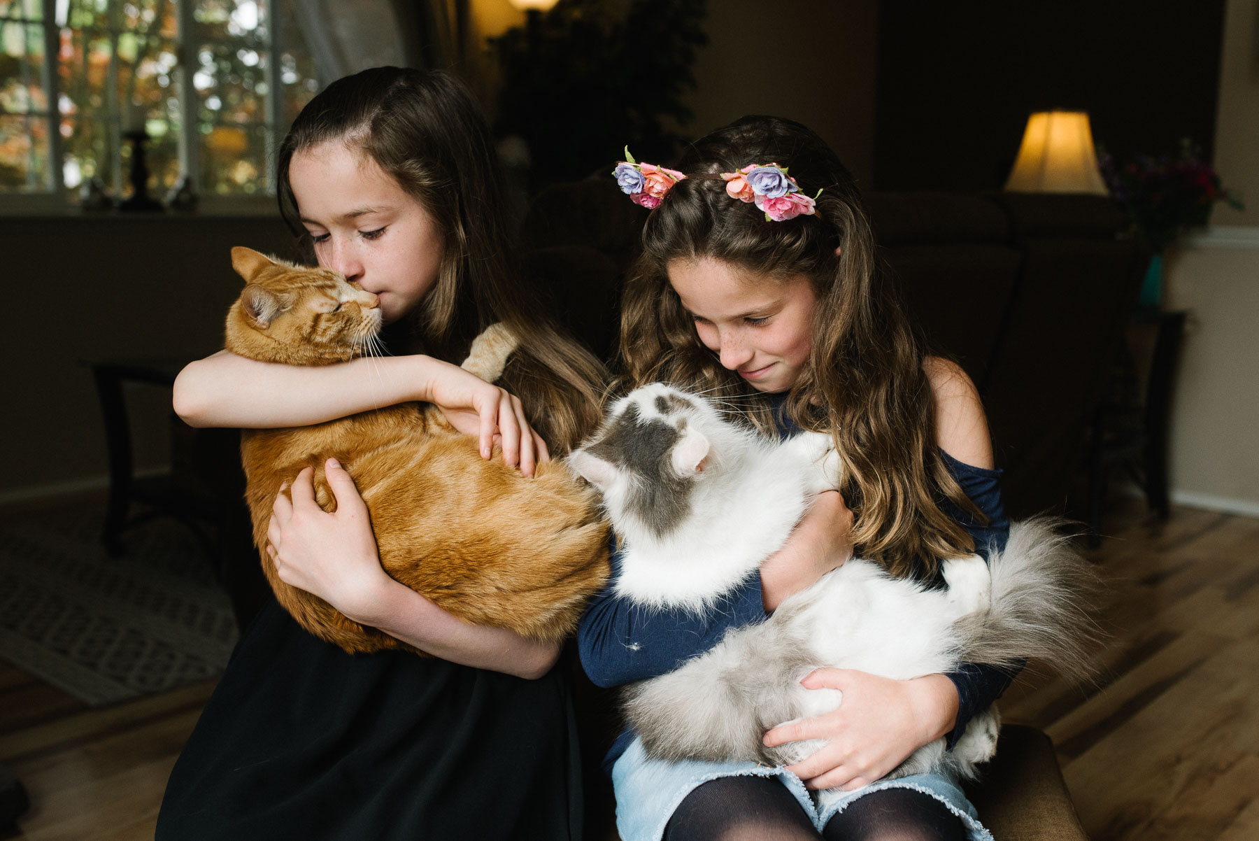 two elementary aged girls cuddle with their two cats