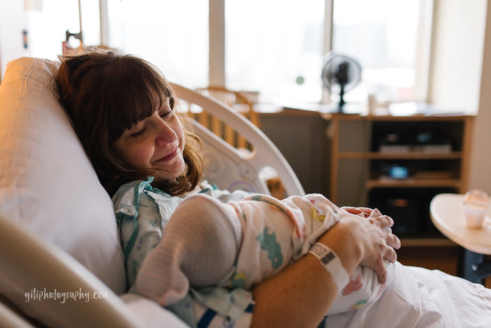 new mother lying in hospital bed looks lovingly at her newborn baby