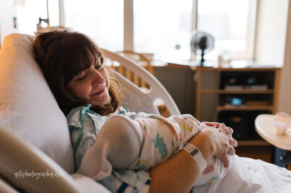 new mother lying in hospital bed looks lovingly at her newborn baby