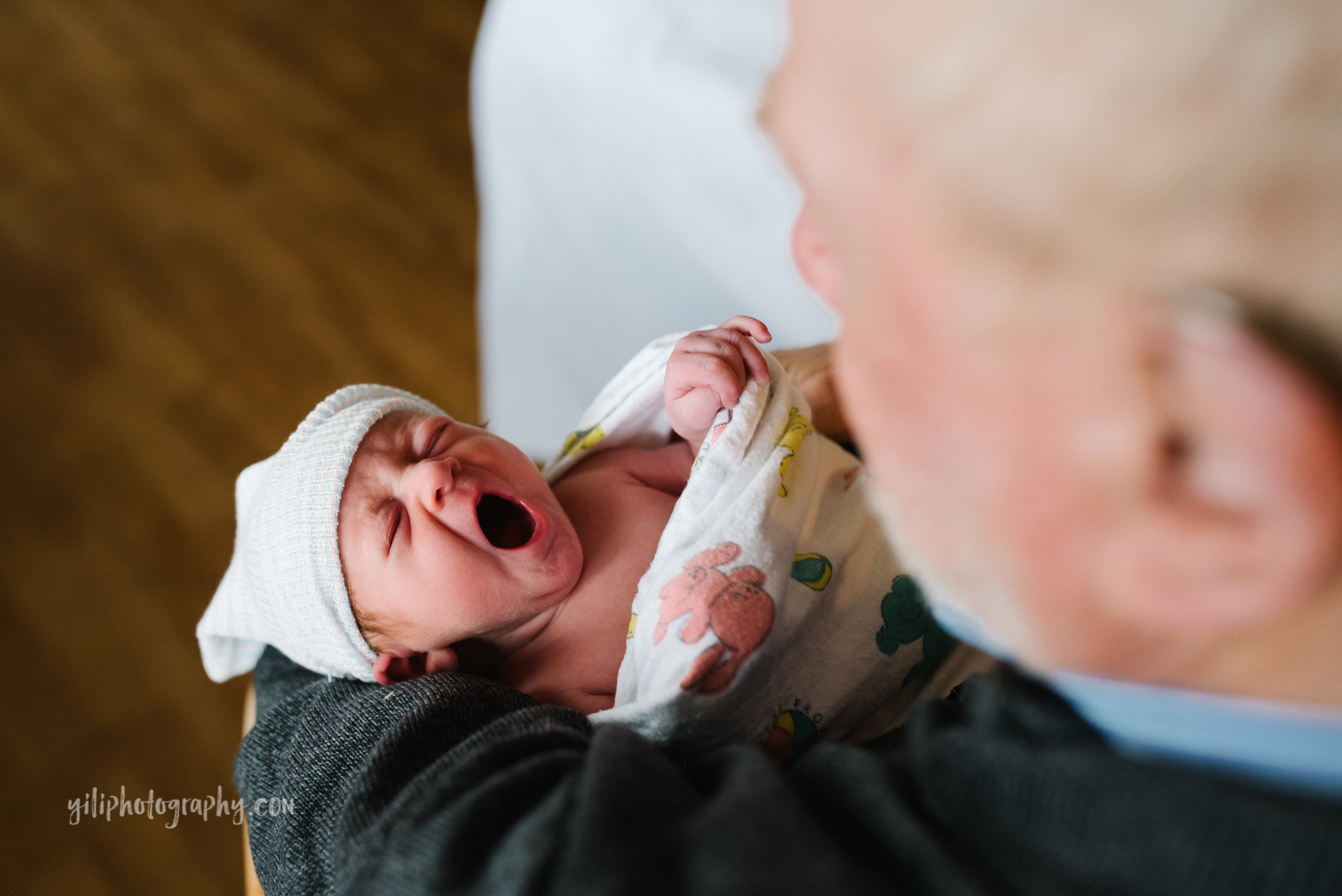 top down photo of newborn baby girl yawning in grandfather's arms