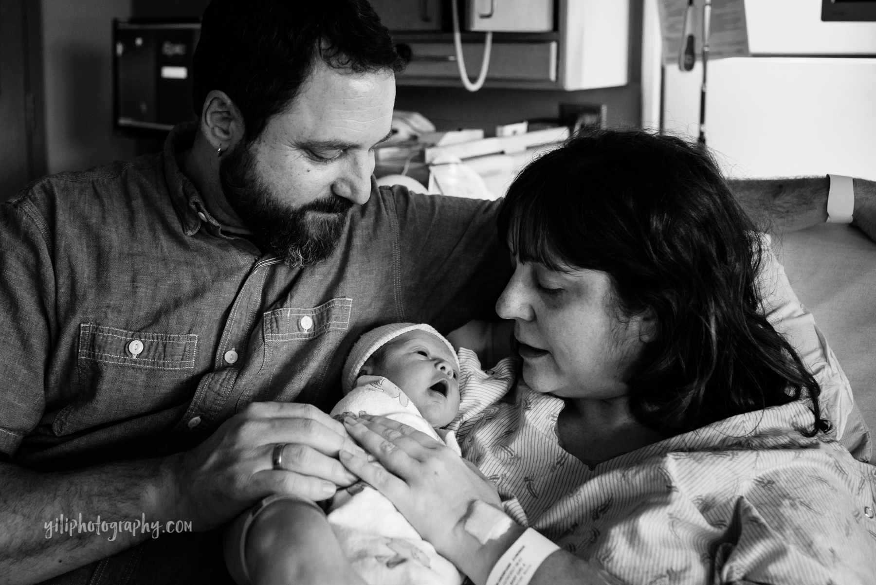 mom and dad cuddling with new baby in hospital bed
