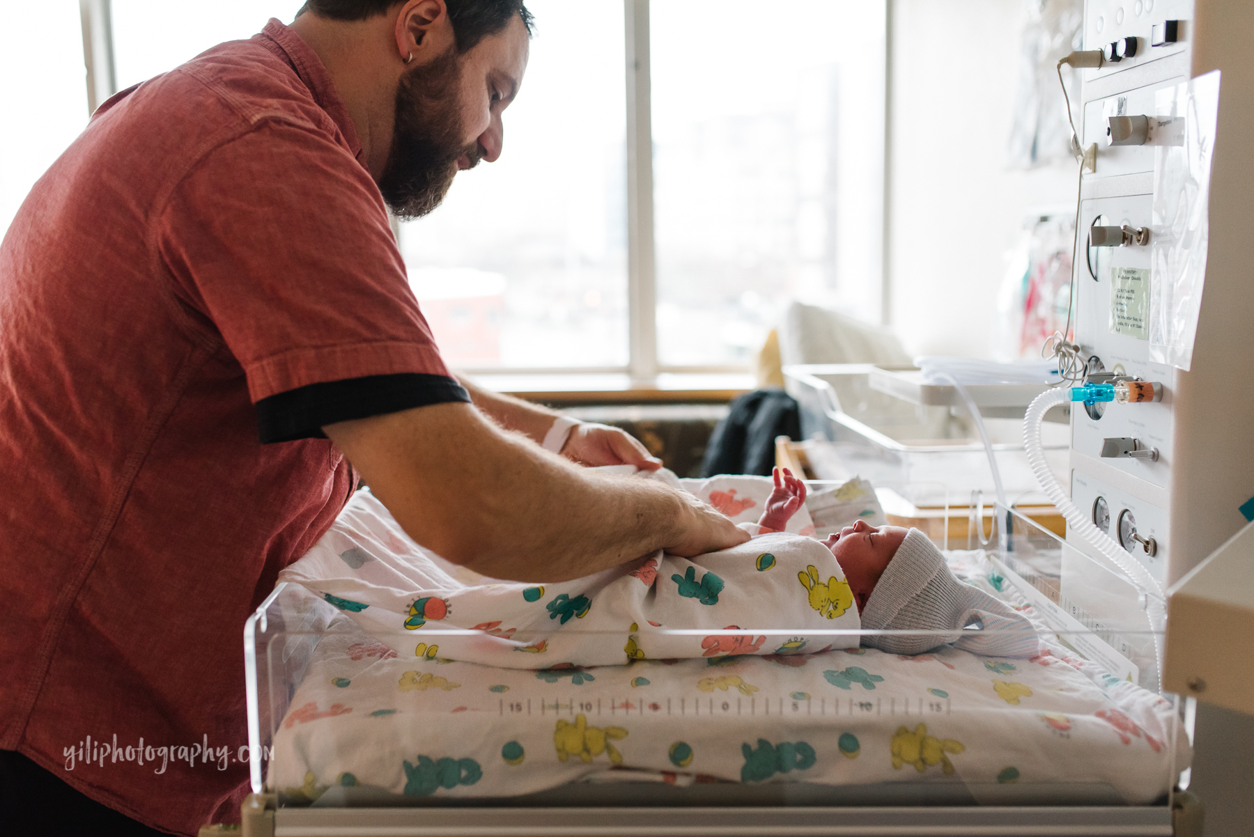 New dad swaddles newborn baby on infant warmer bed