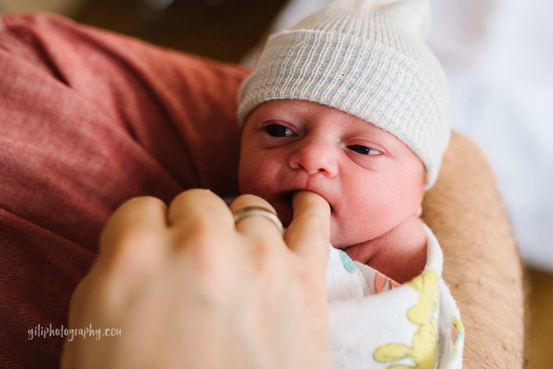 close up of swaddled newborn baby sucking on dad's finger 