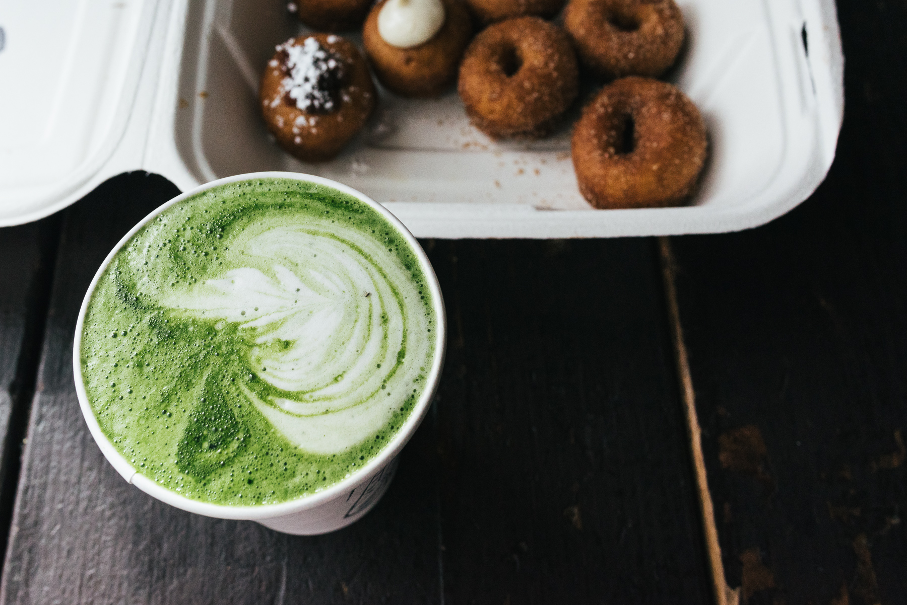 matcha green tea latte with doughnuts in background