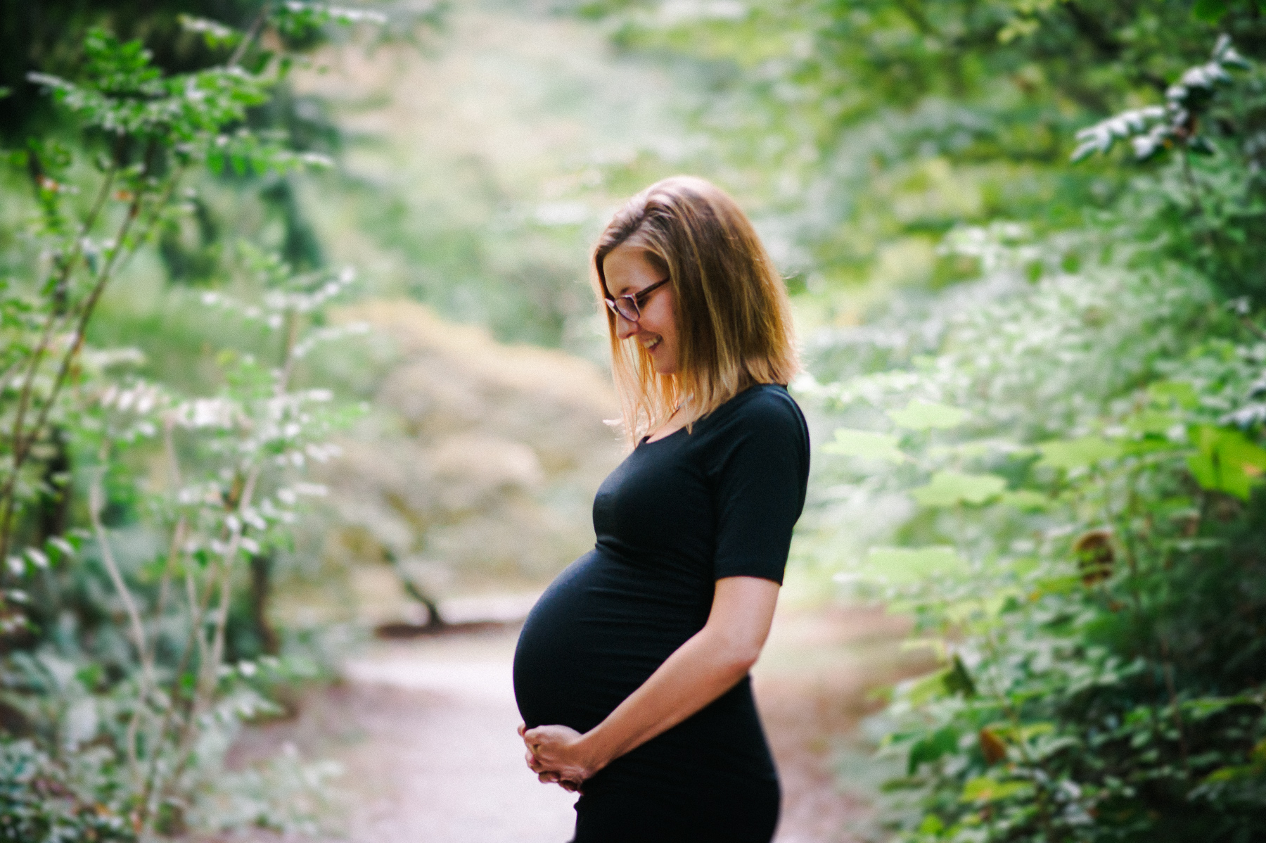 maternity portrait of mother in black dress among foliage 