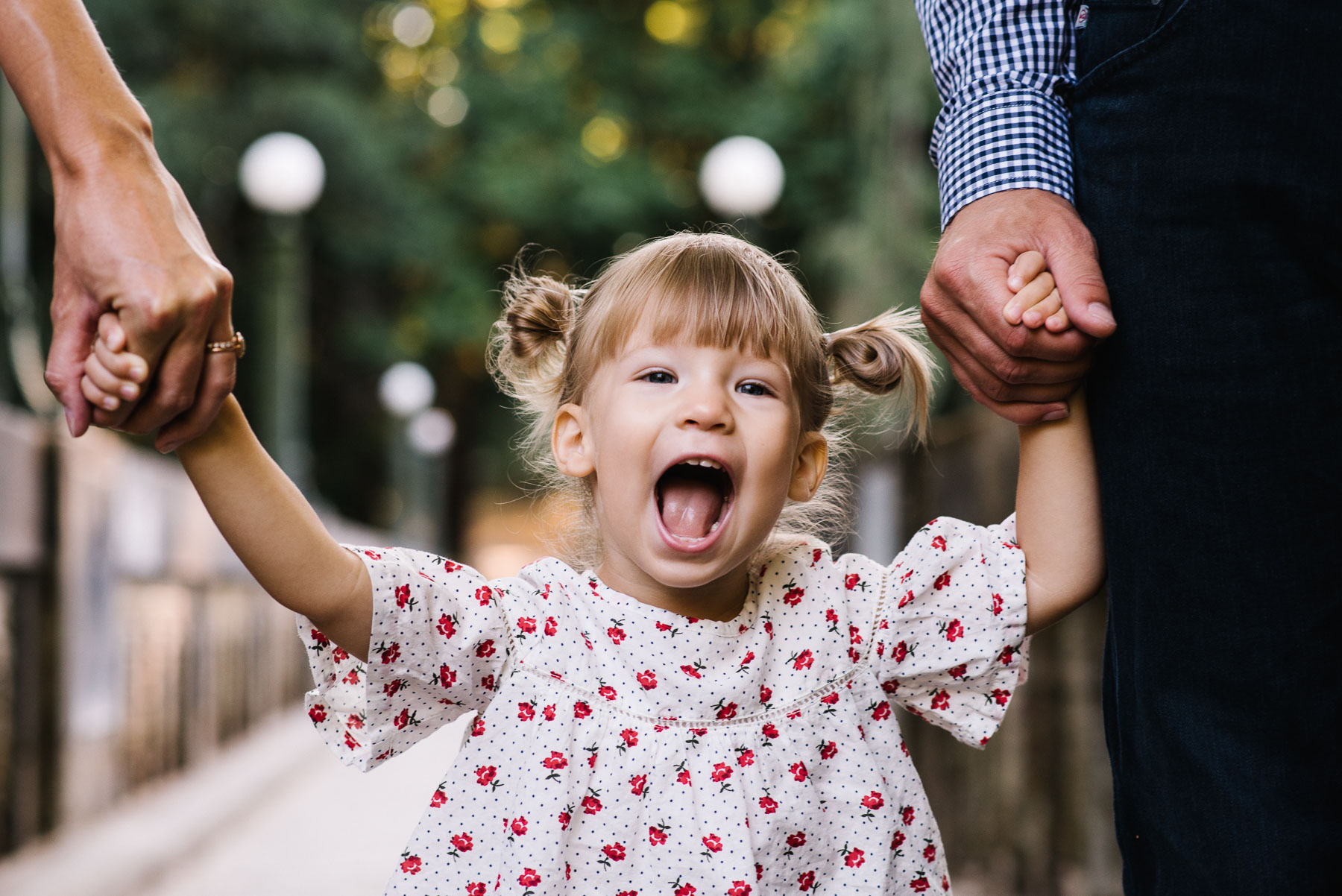 two year old with wide smile holding parents hands in washington park arboretum seattle