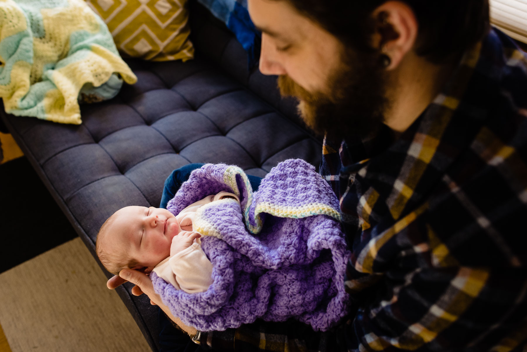 father sitting on couch holding newborn baby girl